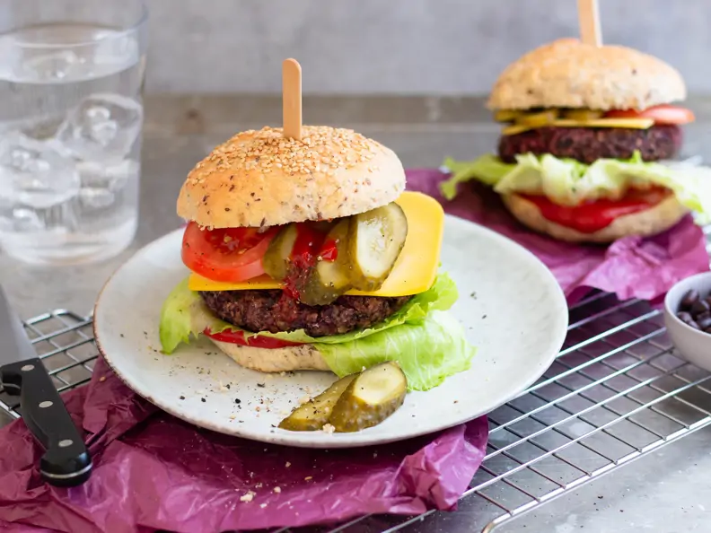 Veganer Cheeseburger mit saftigem Black Bean Patty auf pinkem Papier