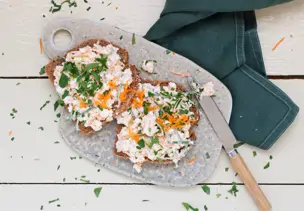 Zwei Brotscheiben mit weißem Frischkäse liegen auf einem Brett