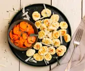 Low-Carb-Gnocchi auf dunklem Teller, daneben dunkle Schale mit gegarten Möhrenscheiben