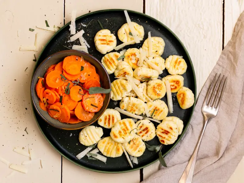 Low-Carb-Gnocchi auf dunklem Teller, daneben dunkle Schale mit gegarten Möhrenscheiben