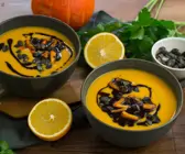 Orange-leuchtende Kürbissuppe in dunklen Schälchen