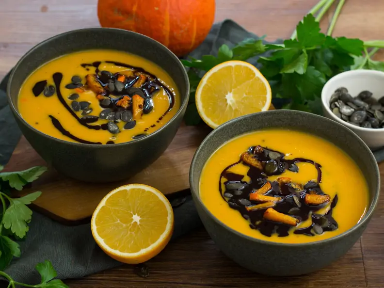 Orange-leuchtende Kürbissuppe in dunklen Schälchen