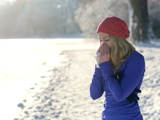 Junge Frau in sportlicher Kleidung im Schnee putzt sich die Nase