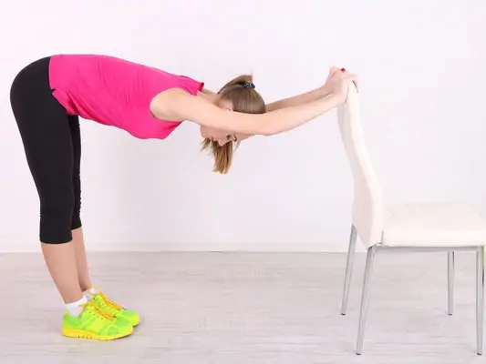 Frau stretcht ihren Rücken mit Hilfe eines Stuhls