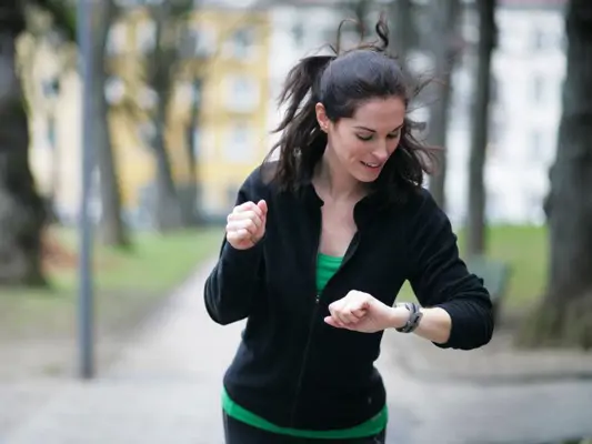 Dunkelhaarige Frau schaut beim Joggen auf ihre Uhr