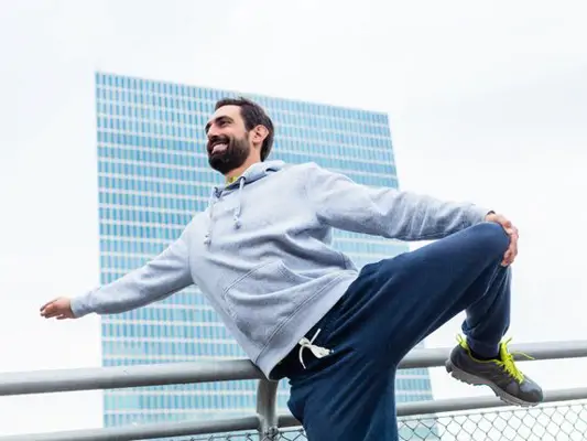 Mann macht Stretch-Übungen vor einem großen Hochhaus 