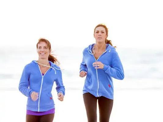 Zwei Frauen mit blauen Trainingsjacken joggen am Strand