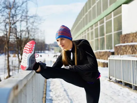 Junge Frau beim Stretching nach dem winterlichen Joggen durch den Schnee 
