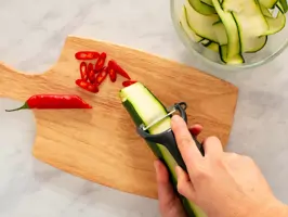 Zucchini wird mit einem Sparschäler in feine Scheiben geschnitten