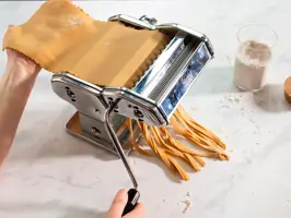 Teig wird in einer Nudelmaschine zu Tagliatelle geschnitten