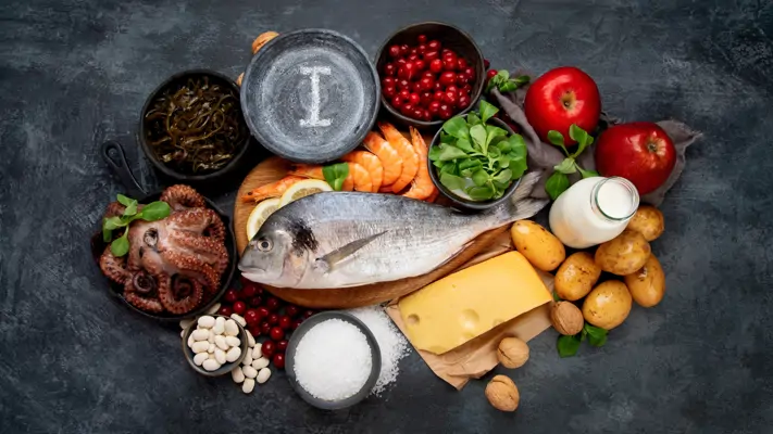 Seefisch, Garnelen, Oktopus, Salz, Käse, Milch, Kartoffeln, Äpfel auf dunklem Untergrund