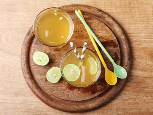 Zwei Gläser Ginger Ale mit Strohhalm und Limette auf einem runden Holzbrett