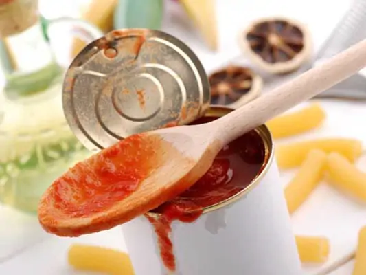 Eine geöffnete Dose Tomaten mit einem Kochlöffel