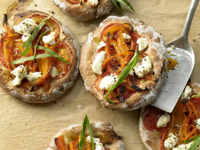 Kleine, runde Pizzen auf einem mit Backpapier ausgelegtem Blech