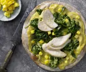 Pizza auf indische Art mit Hähnchen auf einem grauen Untergrund, daneben eine Schale mit Mangowürfel