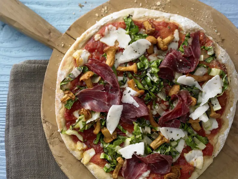 Kartoffelpizza mit Pfifferlingen auf einem runden Holzbrett