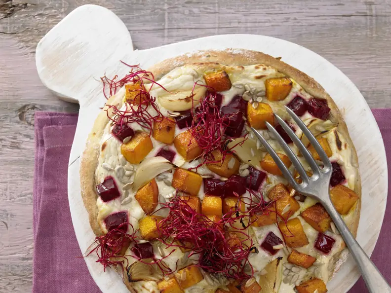 Pizza mit roter Bete auf einem Holzbrett und einer Gabel