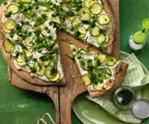 Grüne Pizza auf einem Holzbrett, ein Stück angeschnitten 
