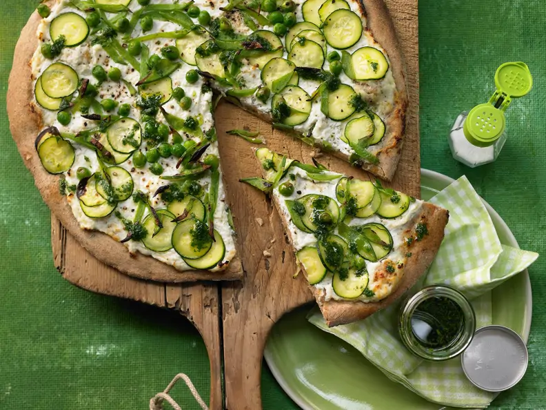 Grüne Pizza auf einem Holzbrett, ein Stück angeschnitten 