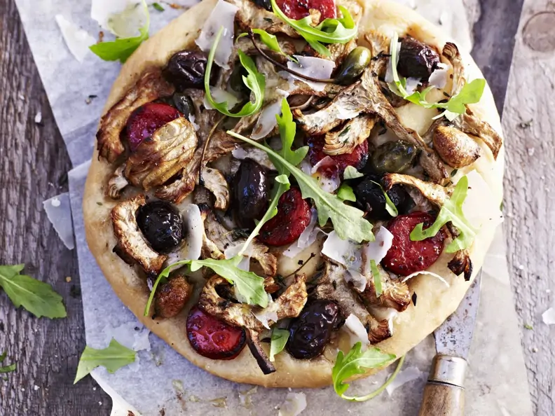 Pizza mit Artischocken, schwarzen Oliven, Rucola und scharfer Wurst (Chorizo)