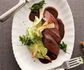 Filet vom Reh neben Kräuterkartoffelpüree auf Rotweinsoße, serviert auf weißem Teller und garniert mit Petersilie