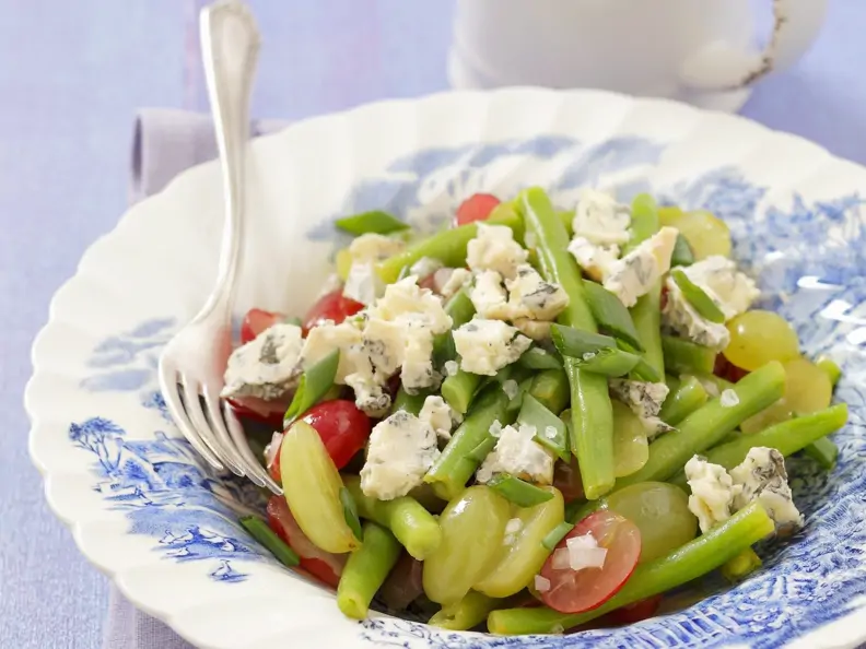 Grüner Bohnensalat mit pikantem Käse und Trauben auf Teller 