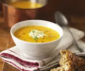 Orangefarbene Suppe in weißer Schale mit weißem Topping