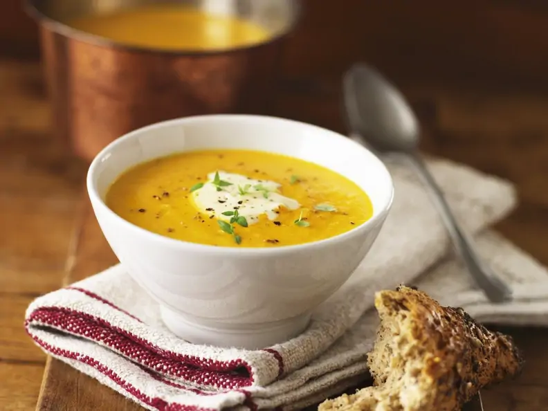 Orangefarbene Suppe in weißer Schale mit weißem Topping