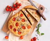 Dinkel-Focaccia mit Zwiebeln, Tomaten und Oregano serviert auf einem Holzbrett