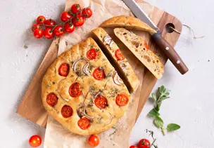 Dinkel-Focaccia mit Zwiebeln, Tomaten und Oregano serviert auf einem Holzbrett