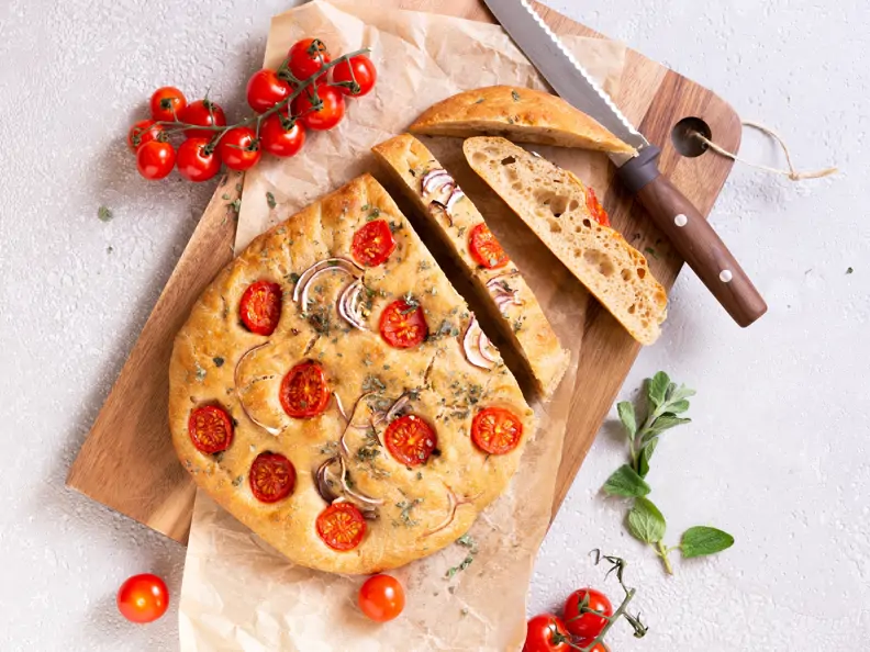 Dinkel-Focaccia mit Zwiebeln, Tomaten und Oregano serviert auf einem Holzbrett