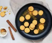 Kleine, runde Plätzchen auf schwarzem Teller, bestreut mit Kurkuma