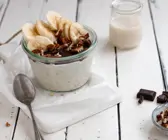 Overnight Oats mit Schokoladenschicht und Bananen-Pekan-Topping serviert in einem Glas 