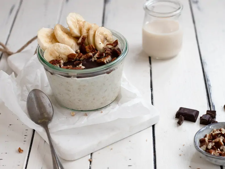 Overnight Oats mit Schokoladenschicht und Bananen-Pekan-Topping serviert in einem Glas 