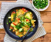 Buntes Couscous-Gemüse auf schwarzem Teller mit Brokkoli, Paprika, Möhren und Schnittlauchröllchen