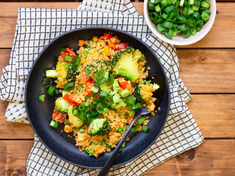Buntes Couscous-Gemüse auf schwarzem Teller mit Brokkoli, Paprika, Möhren und Schnittlauchröllchen