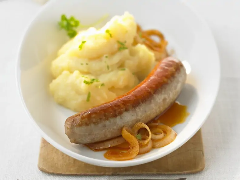Bratwurst mit Kartoffel-Zwiebel-Brei auf einem weißen Teller