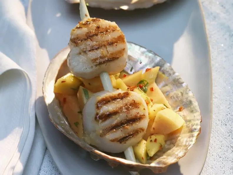 Spießchen mit Jakobsmuscheln auf tropischem Obstsalat