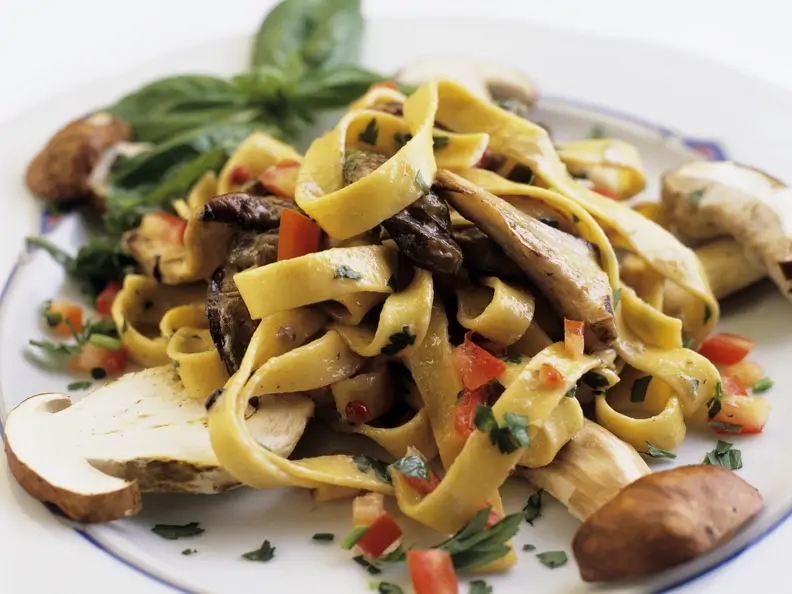Tagliatelle mit Steinpilzen mit Basilikum garniert auf weißem Teller