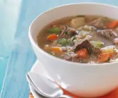 Rindfleisch-Gemüsesuppe mit Graupen in weißer Schale auf blauem Hintergrund