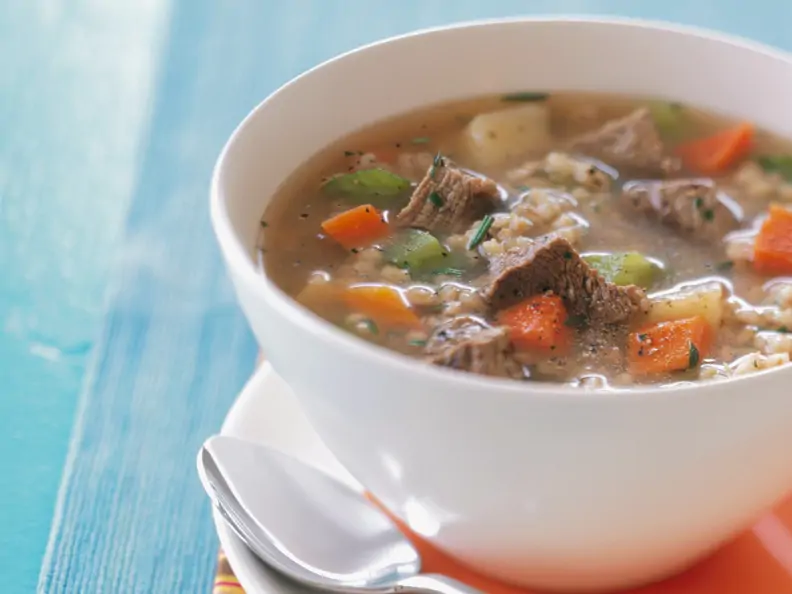 Rindfleisch-Gemüsesuppe mit Graupen in weißer Schale auf blauem Hintergrund