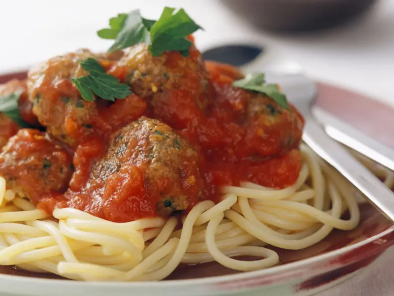 Fleischbällchen in Tomatensauce auf Spaghetti, serviert auf rotem Teller