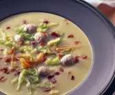 dunkler Teller mit cremefarbener Suppe, buntem Gemüse, Klössen