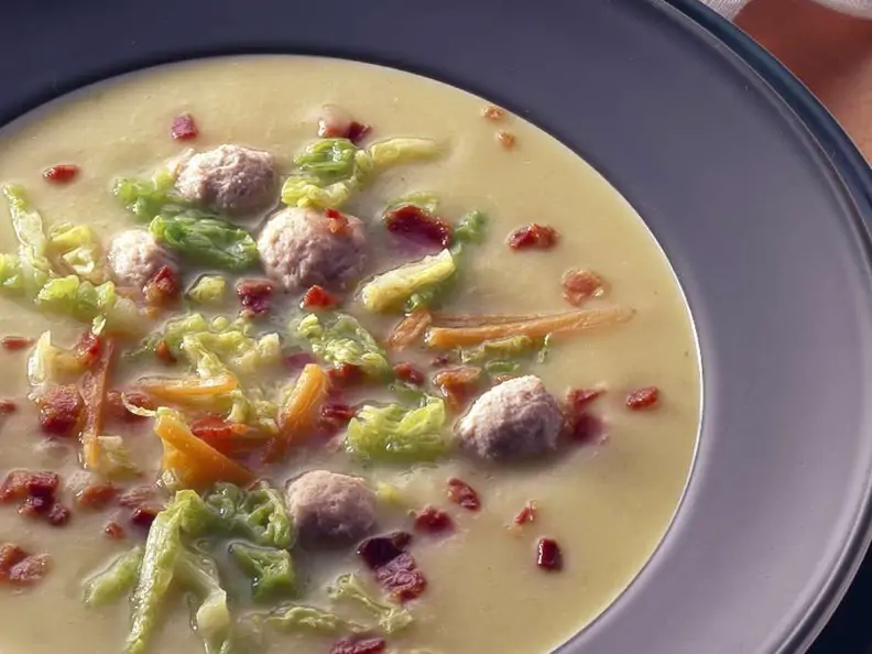 dunkler Teller mit cremefarbener Suppe, buntem Gemüse, Klössen