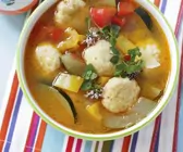 Gemüsesuppe mit Käsebällchen in weiß-grüner Schale auf buntem Set