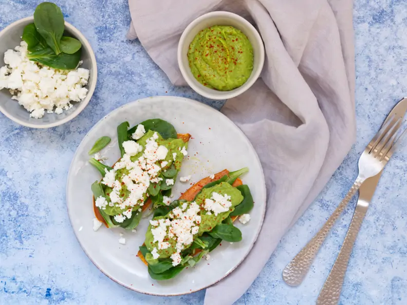 Zwei Süßkartoffelscheiben belegt mit Avocadomus, Feldsalat und Schafskäse