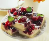 Frischkäse-Beeren-Kuchen Stücke auf Teller mit Zitronenmelisse garniert