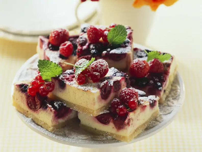 Frischkäse-Beeren-Kuchen Stücke auf Teller mit Zitronenmelisse garniert