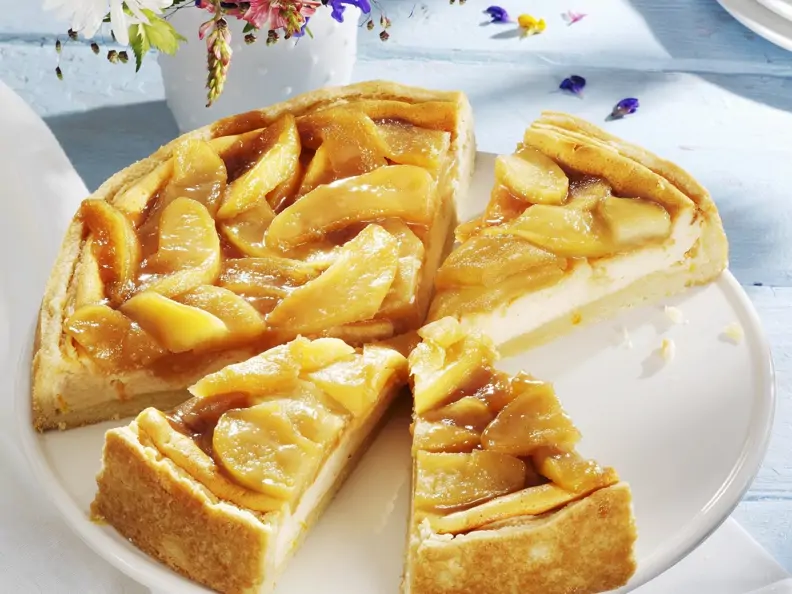 Käsekuchen mit Apfelhaube und Blümchen im Hintergrund