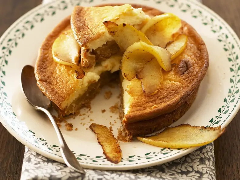 Saftiger Apfel-Käsekuchen mit Boden auf einem hellen Teller mit grünem Dekor